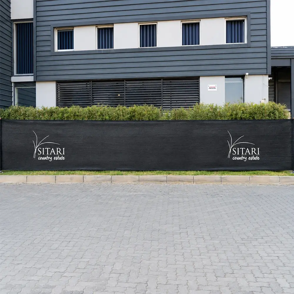 Black branded shade net fencing with two Sitari Country Estate logos installed along a landscaped commercial property.